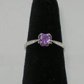 Silver ring with a purple gemstone on a black stand against a gray background