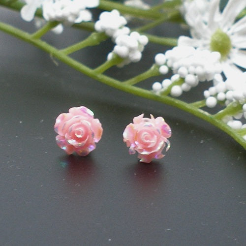 Pink rose-shaped earrings on a dark surface with white flowers in the background