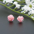 Pink rose-shaped earrings on a dark surface with white flowers in the background