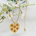 Gold heart-shaped pendant with embedded stones on a gold chain, displayed against a white background with greenery.