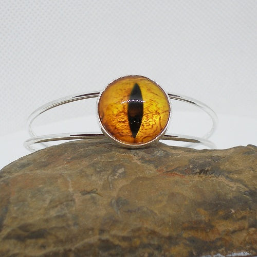 Silver cuff bracelet with a dragon eye on a stone surface