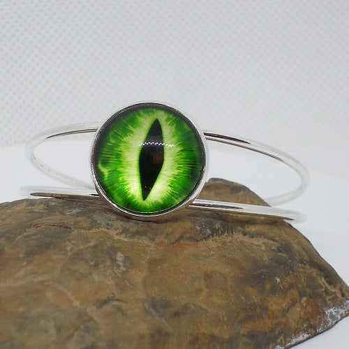Cuff Bracelet with a green eye design on a stone surface