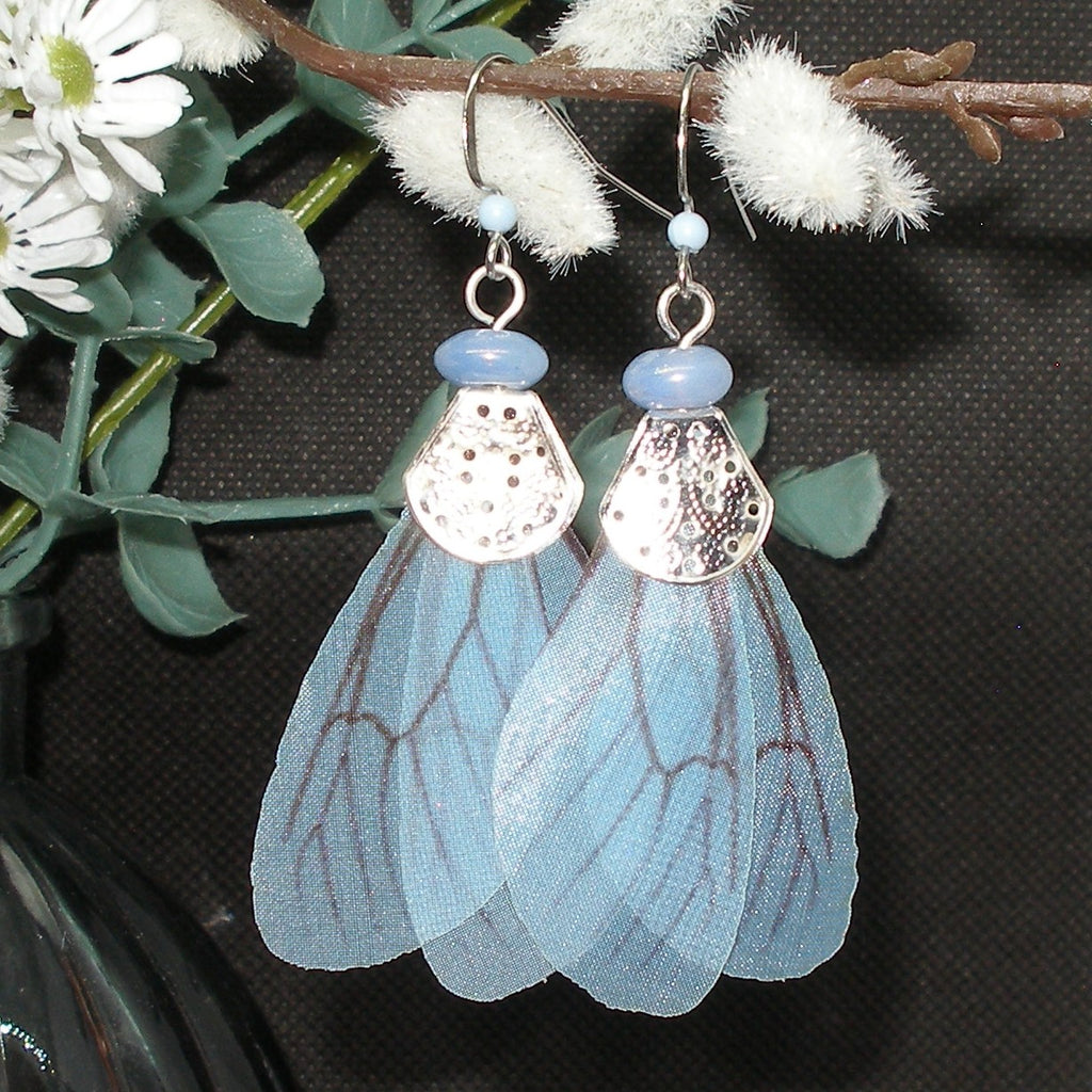 Blue fairy wing earrings with silver accents on a dark background
