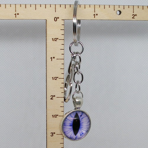 Silver keyring with a purple eye-shaped pendant next to a ruler for scale on a gray background