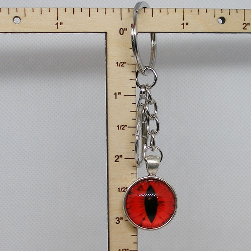 Keychain with red and black eye design next to a ruler on a gray background