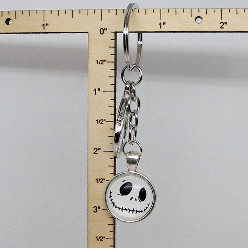 Keychain with a circular pendant featuring a face design, next to a ruler for scale on a gray background.