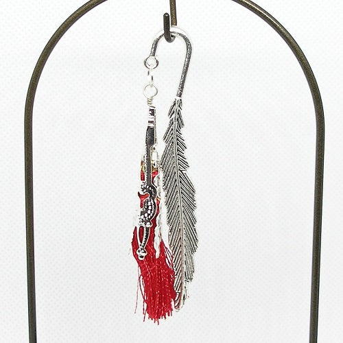 Feather shaped metal bookmark with red tassel on a white background