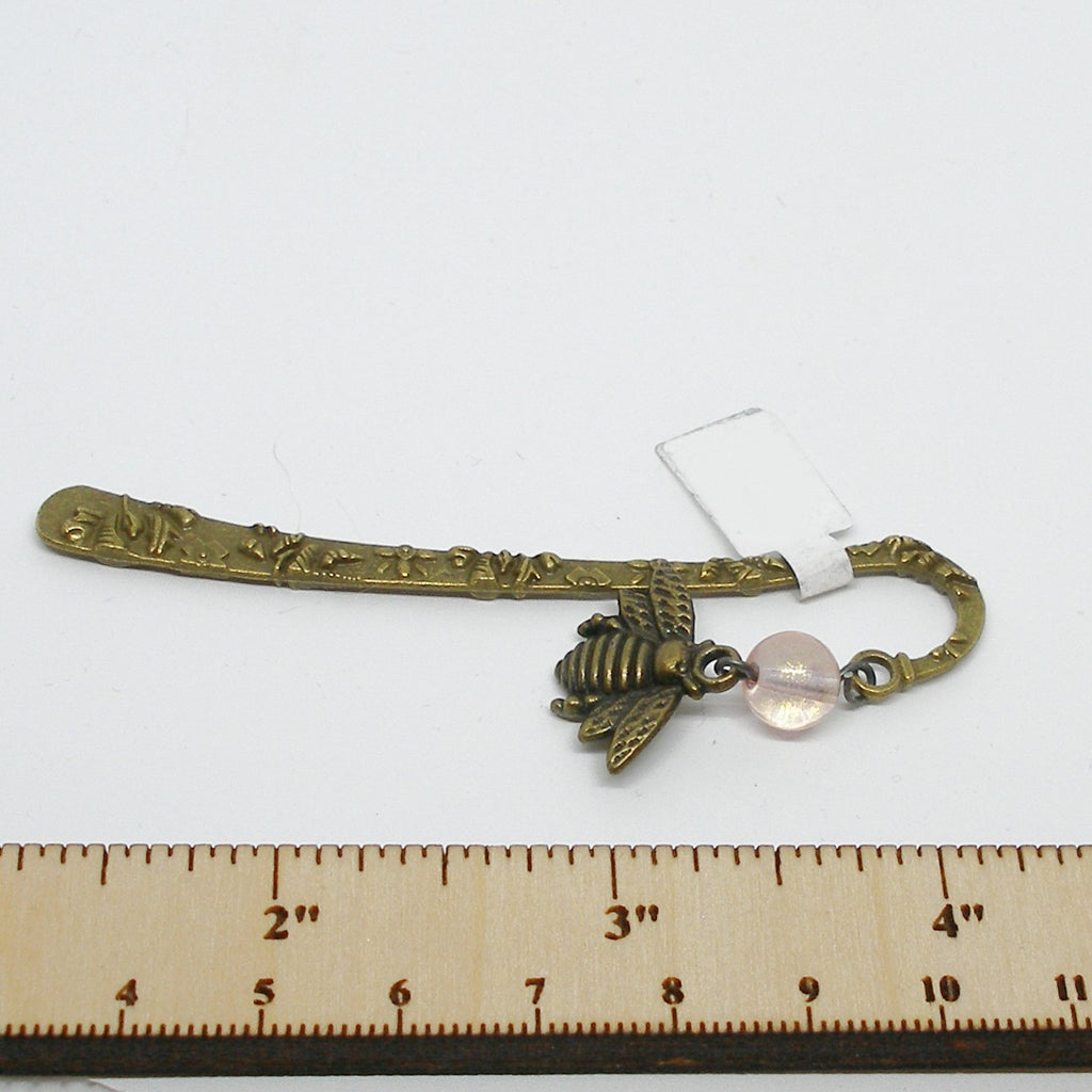 Decorative brass bookmark with bee charm and pink bead on a white background