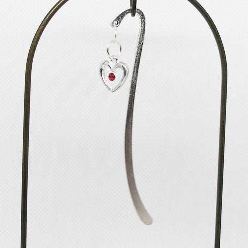 Silver heart-shaped metal bookmark with a red gemstone on a white background