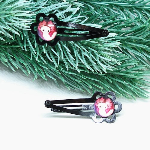 Two hair clips with an axolotl design on a green branch background