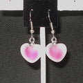 Heart-shaped earrings with pink and white design on a black card.