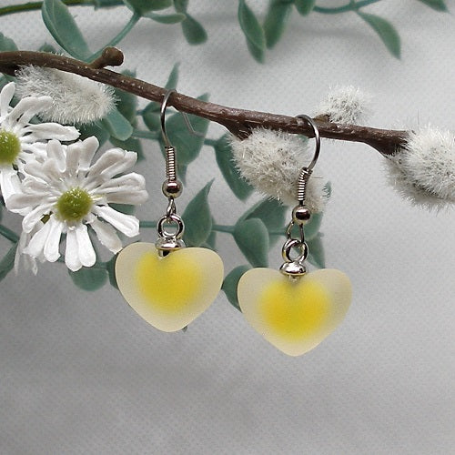 Heart-shaped yellow earrings on a branch with white flowers and green leaves.