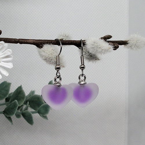 Heart-shaped earrings with purple centers on a branch with white flowers and green leaves.