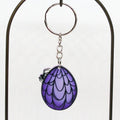 Keychain with purple and black goth egg with spider and web design on a white background