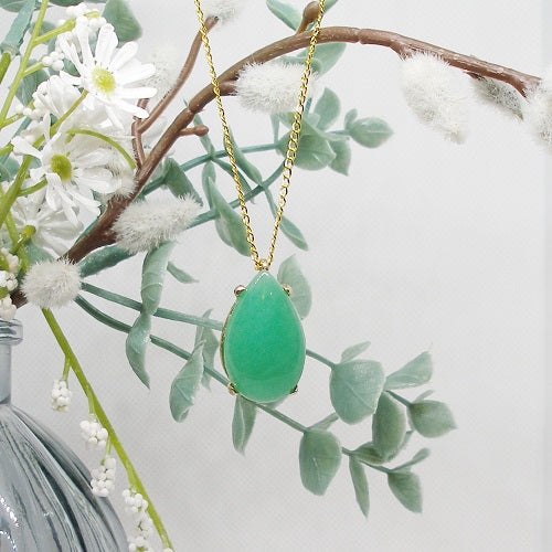 Green teardrop pendant necklace on a gold chain with white flowers and green leaves in the background