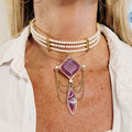 Pearl choker with purple pendant and gold chains worn by a person
