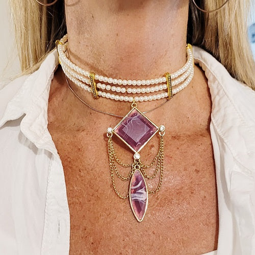 Pearl choker with purple pendant and gold chains worn by a person