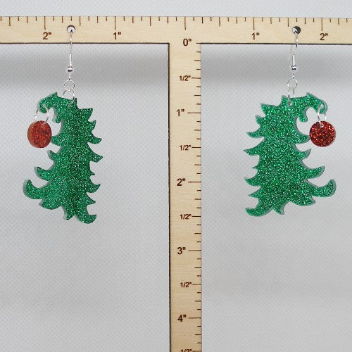 Green glittery Christmas tree earrings with red ornament on a gray background with a ruler for scale.