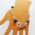 Silver bracelet with dark colored beads on a wooden display