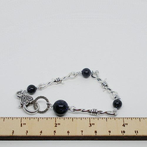 Silver Bracelet with dark color beads on a white background with ruler for scale.