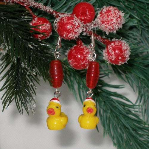 Decorative earrings with yellow rubber duck charms and red beads hanging on a Christmas tree branch.