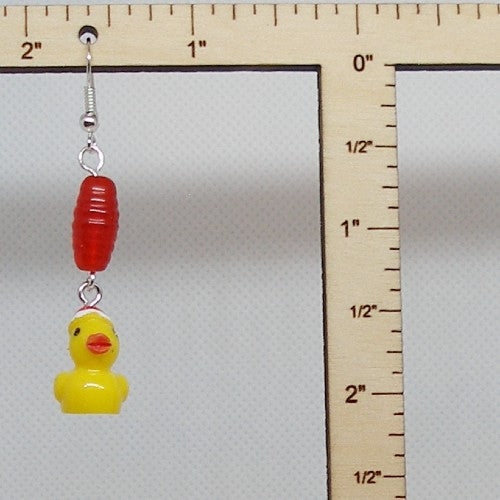 Dangle earrings with a red bead and yellow rubber duckie on a white background with a ruler for scale.